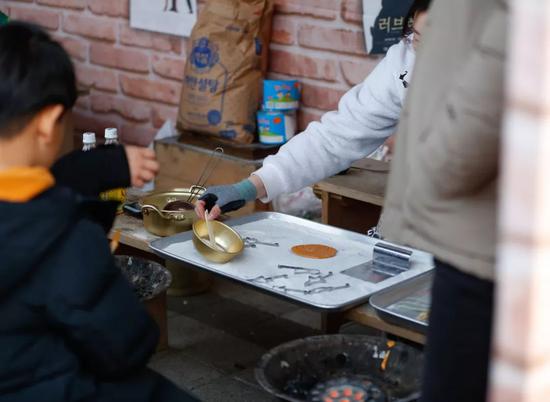 2月5日，在韩国京畿道龙仁市的韩国民俗村，小朋友观看制作传统的糖饼。新华社记者王婧嫱摄