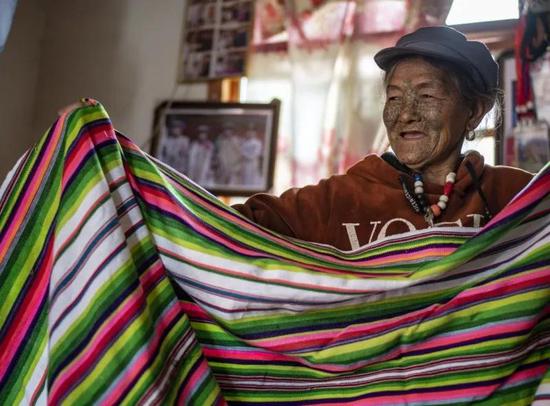 △2019年4月21日，独龙族老人李文仕在家里展示她亲手织的独龙毯