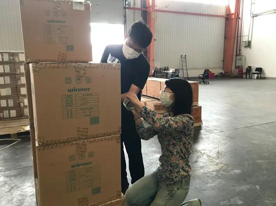 在汉欧班列货仓,魏琛(左)和同事清理即将发送到外国的声援物资,将写着祝愿语的标签贴到纸箱上。