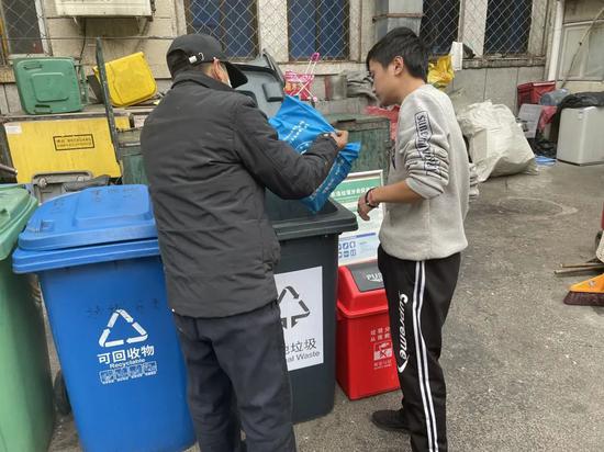 ▲王泽生向一位年轻住户讲解如何正确分类垃圾。 新京报记者 周思雅 摄