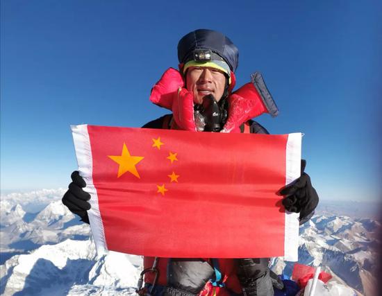 ▲何玉龙登顶珠峰后,举着国旗留影。受访者供图