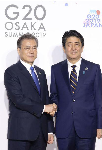 安倍与文在寅握手合影,表情被共同社称“僵硬”。