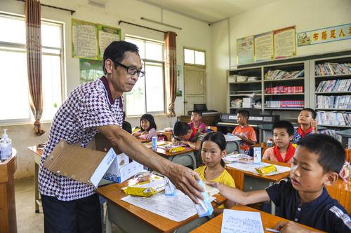  在广西武宣县二塘镇双桂小学，老师韦旭禧给学生们发牛奶（6月19日摄）。新华社记者 曹祎铭 摄