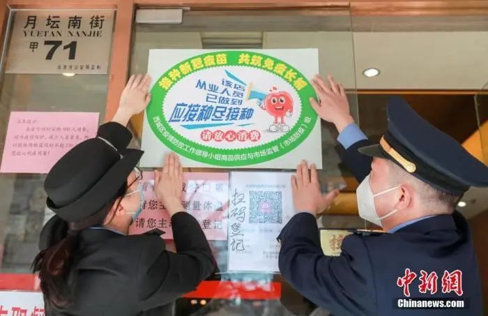2月22日,北京市西城区市场监管局工作人员为同和居(月坛店)张贴“应接尽接”标识。中新社记者 贾天勇 摄