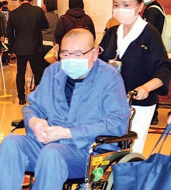 ·刘銮雄戴着口罩，坐在轮椅上。