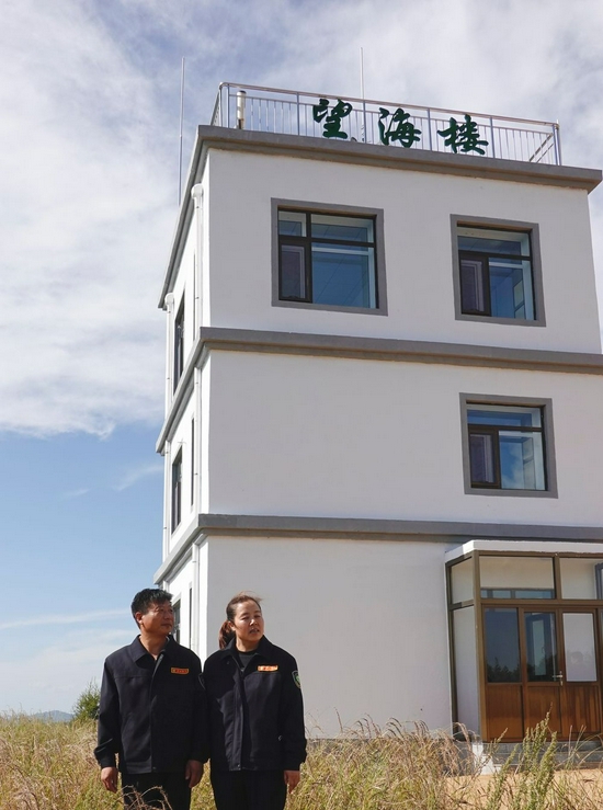 ↑护林员刘军（左）、王娟在塞罕坝机械林场望海楼前（2021年8月23日摄）。在13年的坚守中，刘军、王娟夫妇用常人难以想象的辛勤付出守护林场安全。