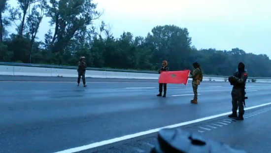武装人员手持摩洛哥国旗，站在公路中间