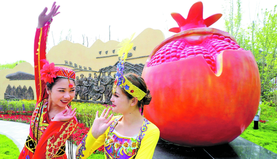 4月29日，两位舞蹈演员在北京世园会新疆室外展园西侧入口处红彤彤的石榴景观造型前翩翩起舞。