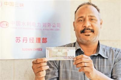 大坝施工人员展示新100苏丹镑纸币，上面是三座大坝的图案。本报记者 苏 航摄