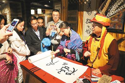 华文媒体代表（右二）在纳西创世纪文化体验中心学写东巴文“福”字。