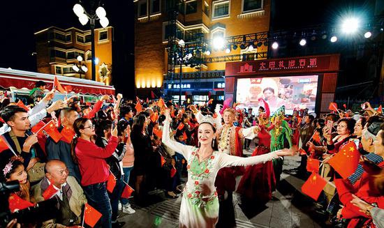 新疆国际大巴扎是新疆商业与旅游繁荣的象征，集建筑、民族商贸、娱乐、餐饮于一体，是新疆旅游业产品的汇集地和展示中心，是“新疆之窗”。图为2018年10月1日，在乌鲁木齐新疆国际大巴扎步行街，歌舞演员和游客一起载歌载舞，欢度国庆。 新疆维吾尔自治区党委宣传部供图
