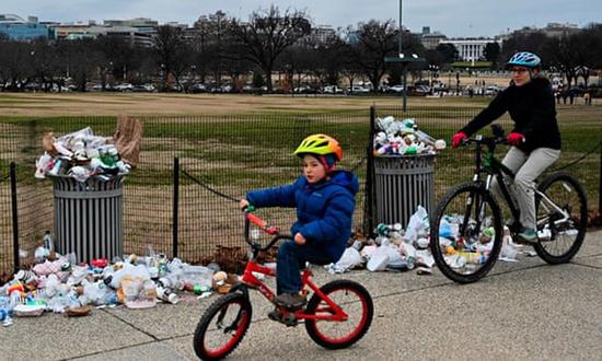 在华盛顿的国家广场，人们骑行经过的垃圾桶周边垃圾散落满地。