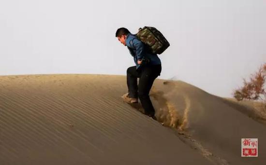 新华社记者赵戈背着器材爬上一座沙丘。