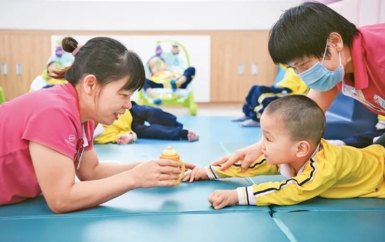 图为2021年4月27日，广东省茂名市社会福利中心工作人员在跟孩子互动交流。该中心现有服务对象806人，其中孤残儿童282名，是一家集养、治、教、娱乐、康复、特殊教育功能于一体的综合性福利事业单位，也是全国脑瘫儿童康复训练示范基地。 新华社记者 邓华/摄