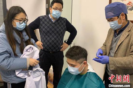 赴武汉前,陆超的未婚妻和同事注视着陆超剪头发。 张斌 摄