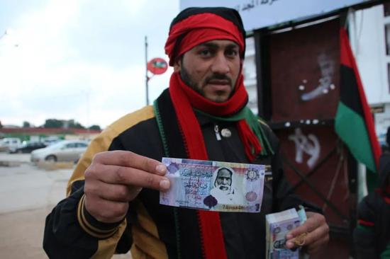 图中纸币中的老者为：利比亚民族英雄奥马尔·穆赫塔尔，卡扎菲的崇拜的革命前辈和精神领袖。1931年，意大利法西斯占领者当着两万多利比亚百姓的面，将被俘的穆赫塔尔绞死。