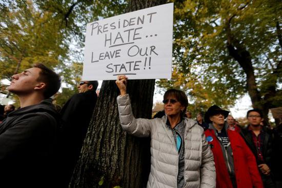 一名抗议者高举标语牌“欢迎”特朗普，标语牌上内容为“仇恨的总统……离开我们的州！！”（路透社）