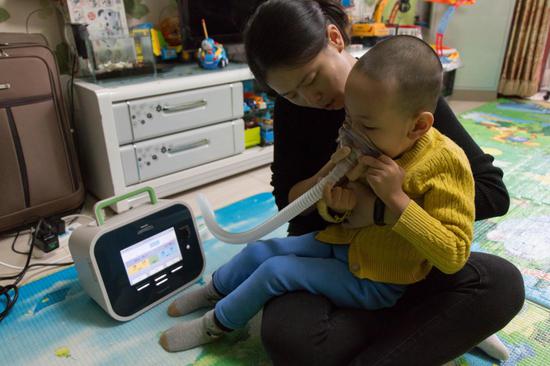 △  2018年10月15日，北京市通州区，松子在使用咳痰机，每次做三组，一组三个，重复吸、咳动作。机器刚到的时候松子爸妈自己试用了一下，“就像把空气‘砰’一下打到肺里，别提多难受了。”咳痰机对脊髓性肌萎缩症患者来说是救命机，一台新品咳痰机售价在30000人民币左右。