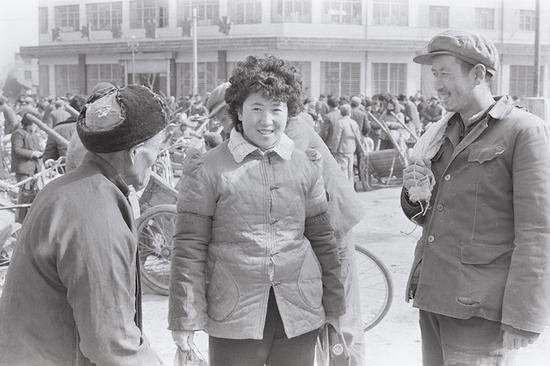 1993年，陕西陇县，街头一男子和老汉围看一位烫头发的妇女。一个普通农村女人烫头发，都能引起男人异样的眼光。摄影|胡武功
