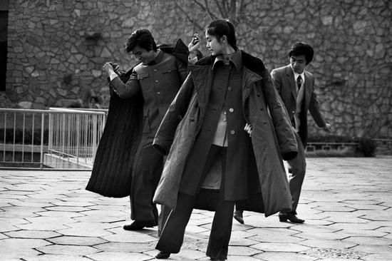 1986年，身披绿色军大衣的年轻人在北京街头跳舞。摄影|郭建设
