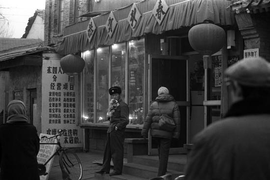 1986年春节，北京东四街头，一个军人手中捧着塑料花在等待意中人。摄影|郭建设