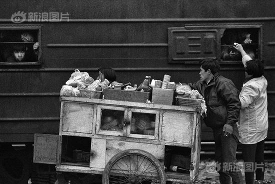1993年1月25日，大年初三。在阜阳火车站广场上经过两天一夜的露天排队，开往上海西站的“闷罐车”农民工专列即将启动，商贩们在“闷罐车”外售卖食品。摄影|于文国