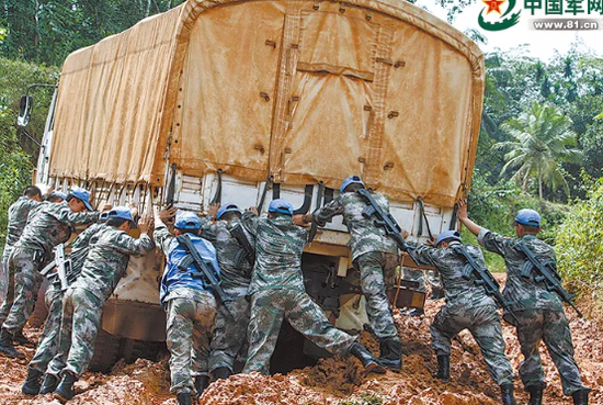 中国赴利比里亚维和部队运输分队官兵在泥泞的道路上推车。