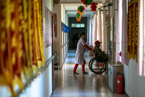 在一家敬老院，一名护理员用轮椅推着一名老人上电梯（2013年10月3日摄）。新华社记者刘金海摄