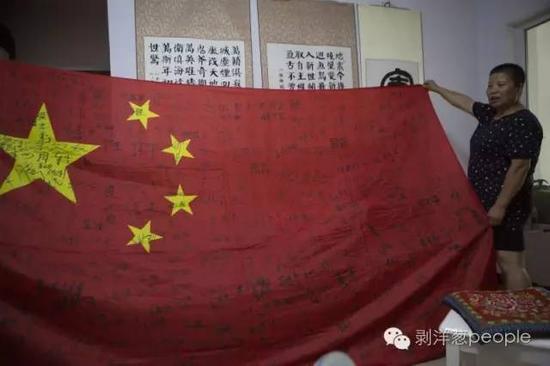 田金芳展示她珍藏的一面国旗，上面签满了她走过的部队中解放军的名字。新京报记者 侯少卿 摄
