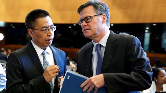 2018年7月26日，中国驻WTO大使张向晨在瑞士日内瓦举行的世界贸易组织会议上与美国驻WTO大使谢伊（右）交谈。