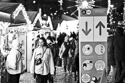 人们在比利时布鲁塞尔的圣诞市场经过一处防疫提示牌供图/新华社