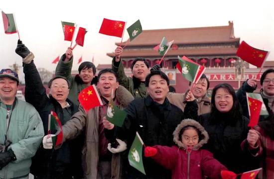 1999年12月20日,澳门回归祖国第一天,北京市民纷纷来到天安门广场庆祝澳门回归。图为北京金洋房产开发有限公司职工挥舞着国旗、澳门特别行政区区旗在天安门前留影。新华社记者 王呈选 摄