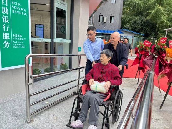 图为一位老年客户在农行达州分行员工和亲人的帮助下经无障碍通道金融营业网点