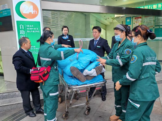 图为农行员工协助救护医生将患病顾客送医救治
