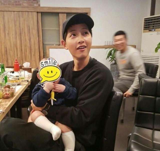 照片中,宋仲基抱着一个很可爱的小孩子.