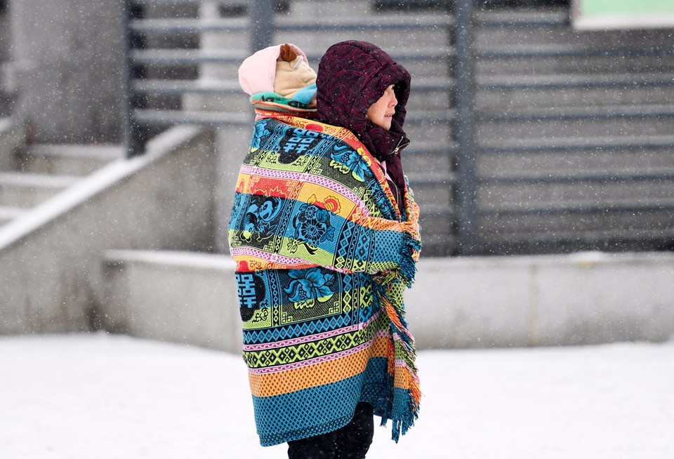 一位奶奶用毛毯裹着孙女冒雪前行.