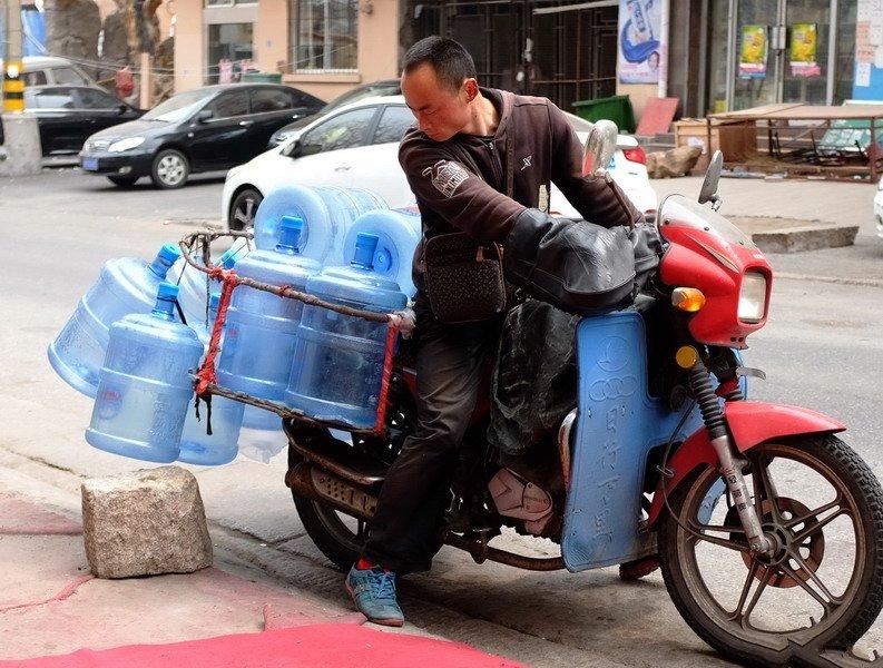 街头这中年男子骑着摩托车运送着矿泉水的空瓶,想必应该是往店里走.
