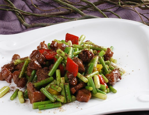 在白色的盘子里,装着一盘羊肉炒蒜苔,味道肯定很好吃.