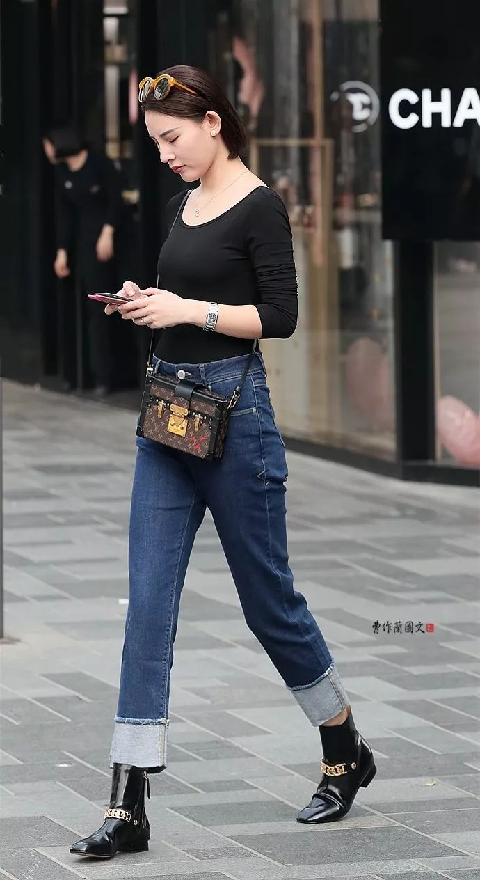 美女穿新款的翻边牛仔裤,黑色亮皮短靴,上身是一件黑色长袖圆领露背