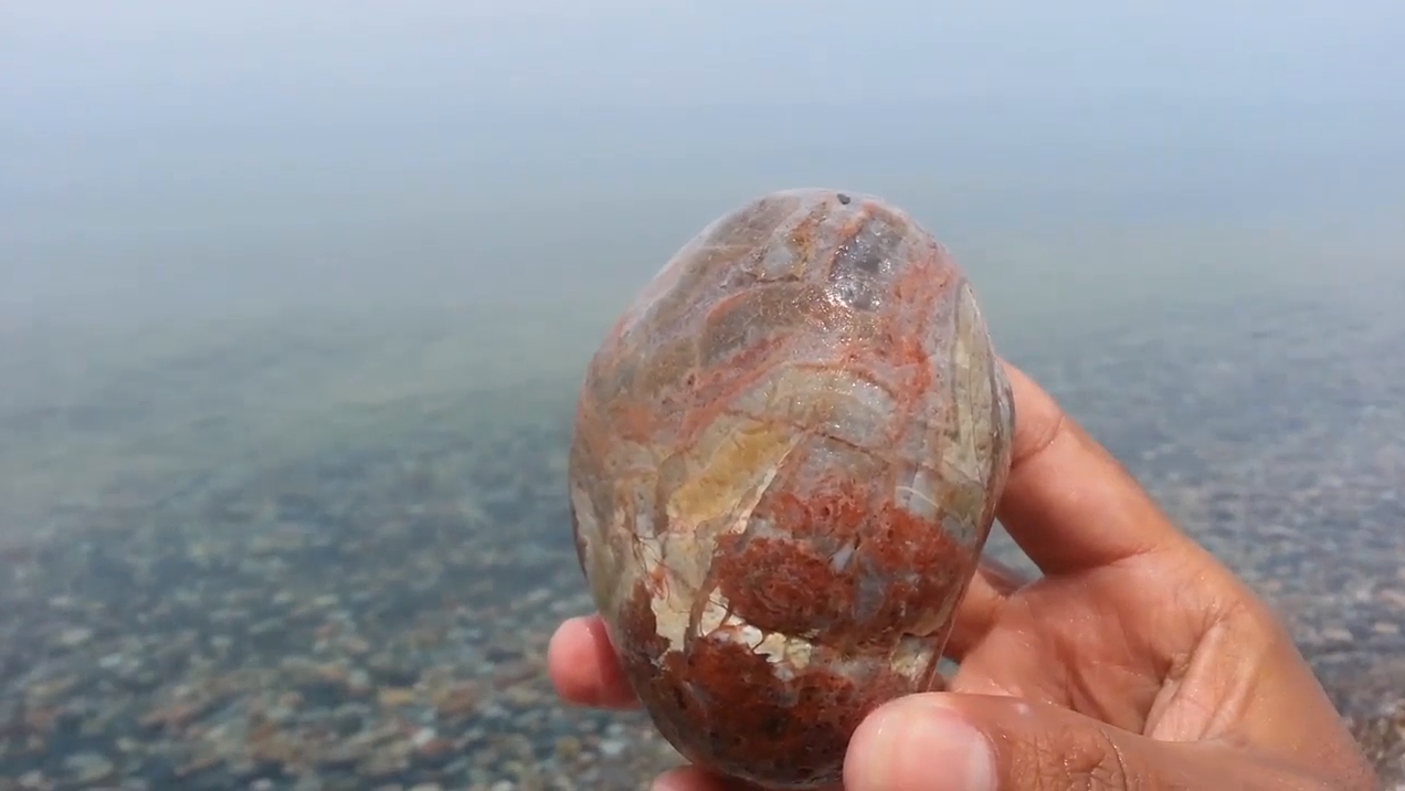 男子湖边游玩,水中捡起一石头,拿着爱不释手