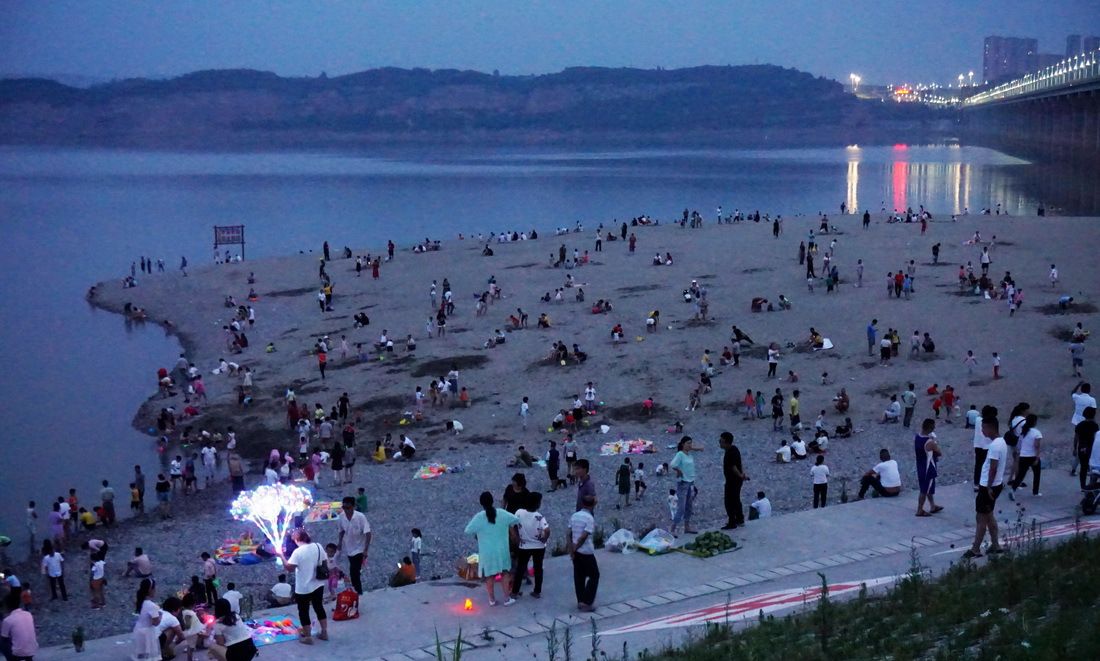 7月13日,湖北省十堰市郧阳区汉江北岸的人造沙滩上游人如织,再现海滩