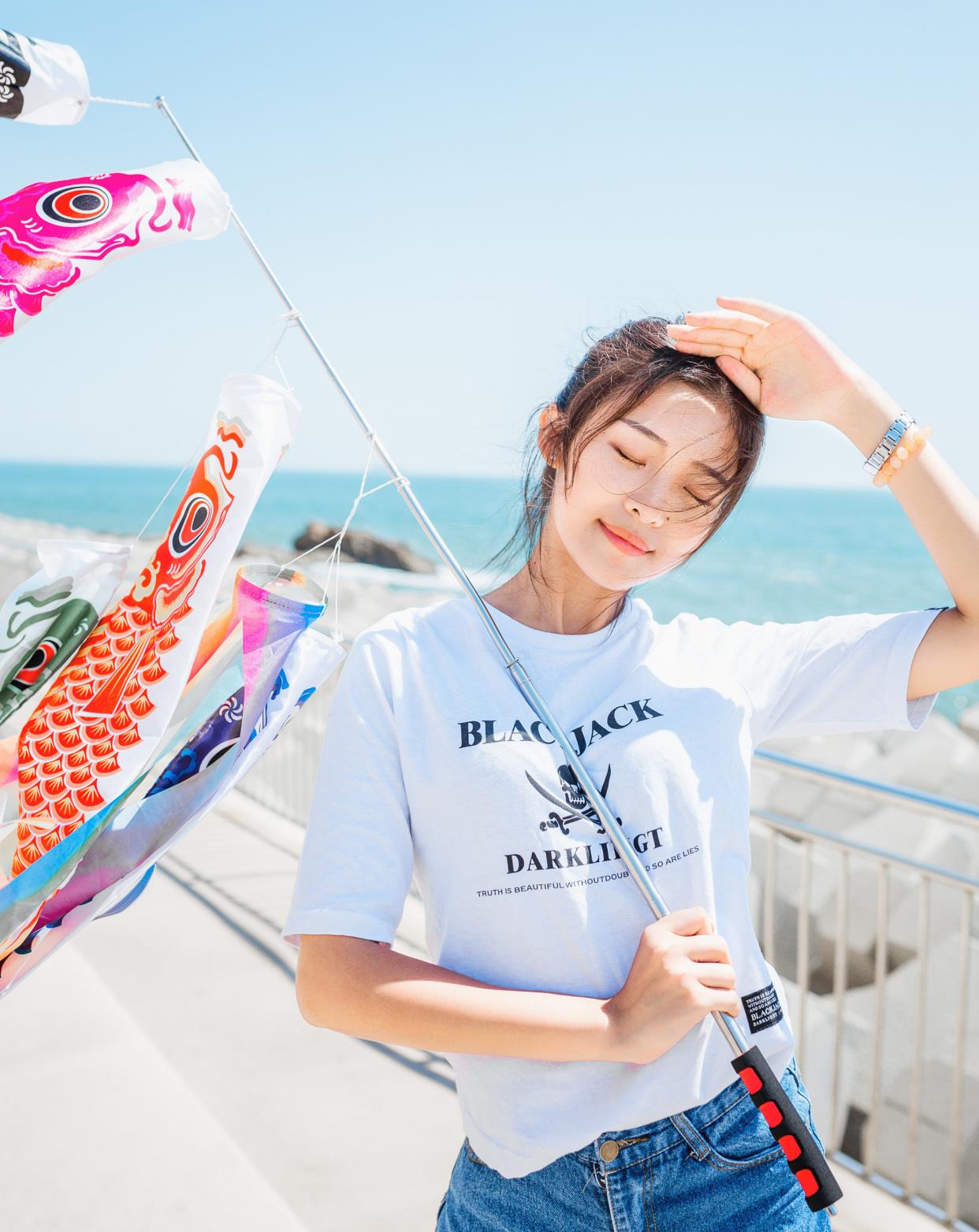 走路上拍照,一只手遮阳,另一只手拿着风筝,闭着眼睛,海风吹乱的发型在