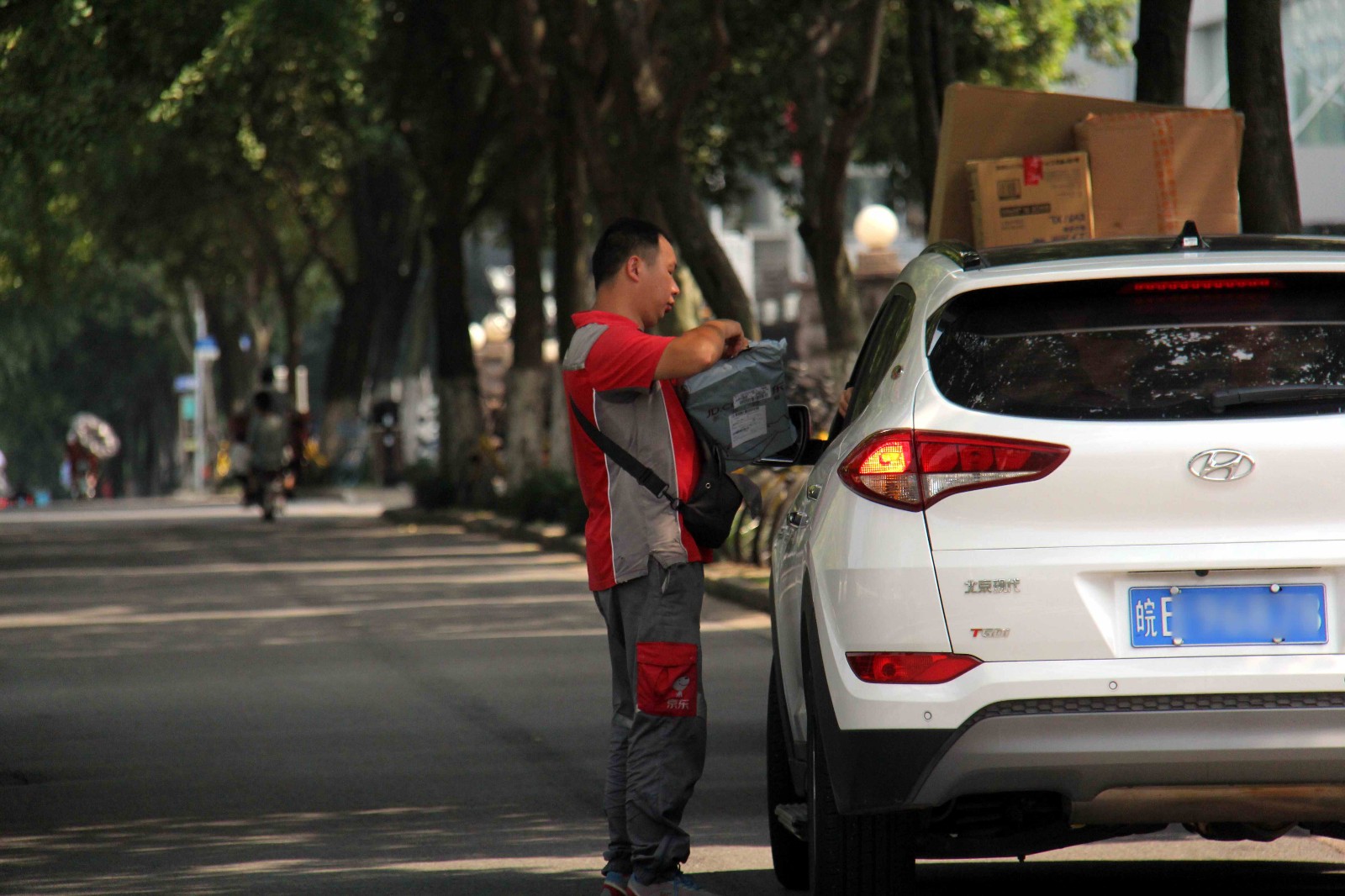 路旁一辆轿车边,一位物流公司的快递小哥正在给一位客户送货,这高温天