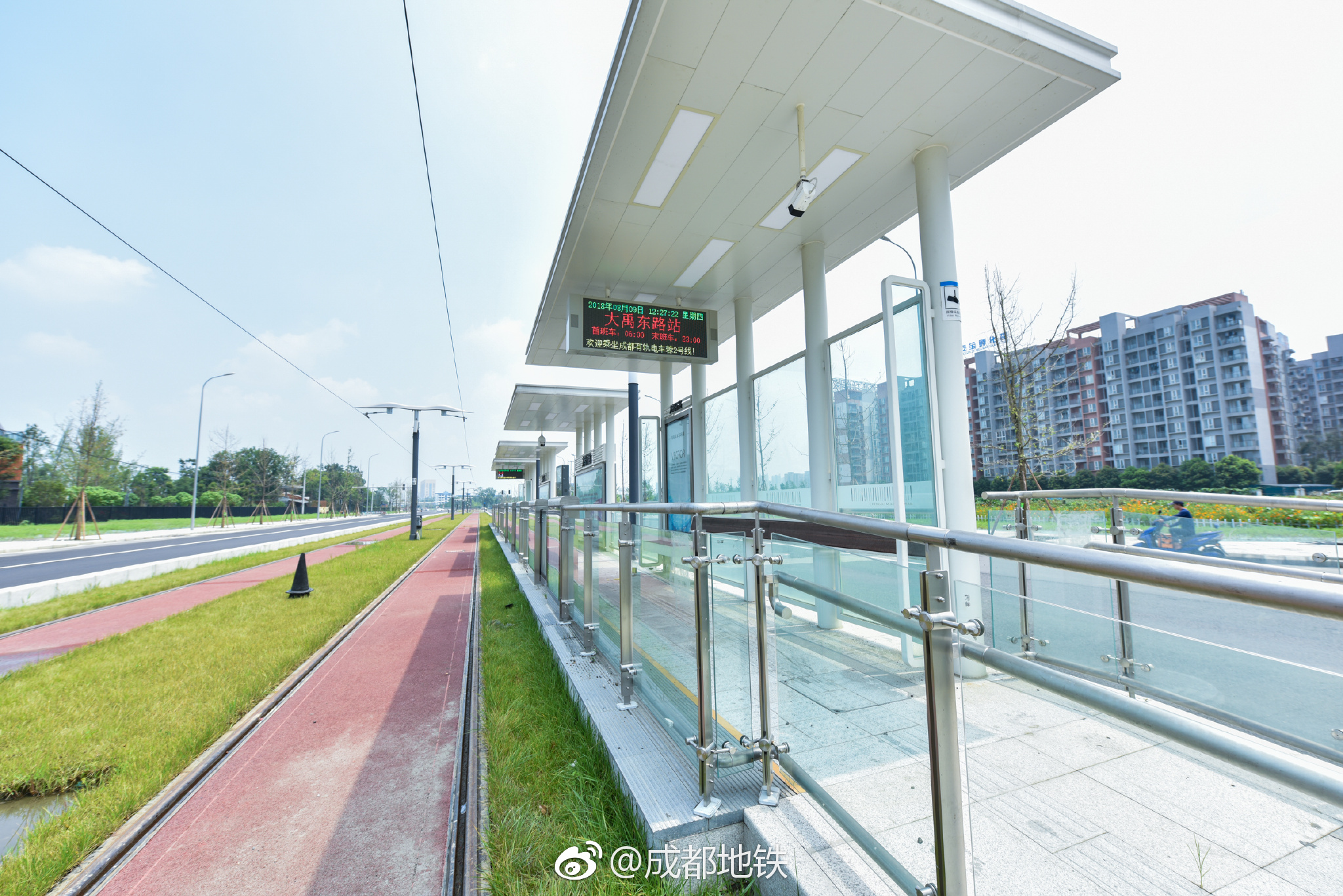 有轨电车蓉2号线车站设置在地面,轨道镶嵌在红色的路面与绿草之间