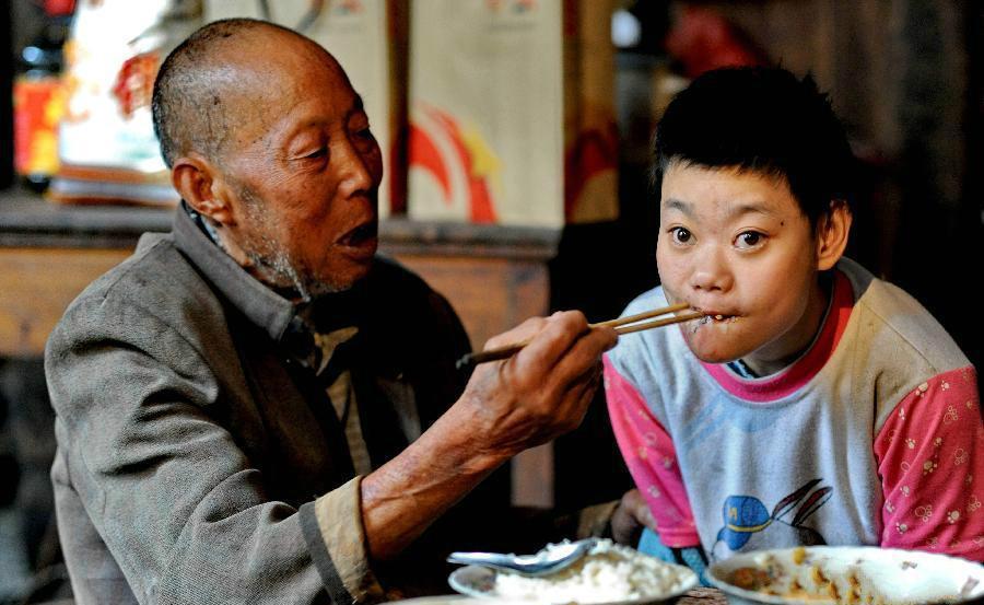 老人正在喂脑瘫的女儿吃饭.妹妹在帮忙照顾姐姐,而老人则在补鞋.