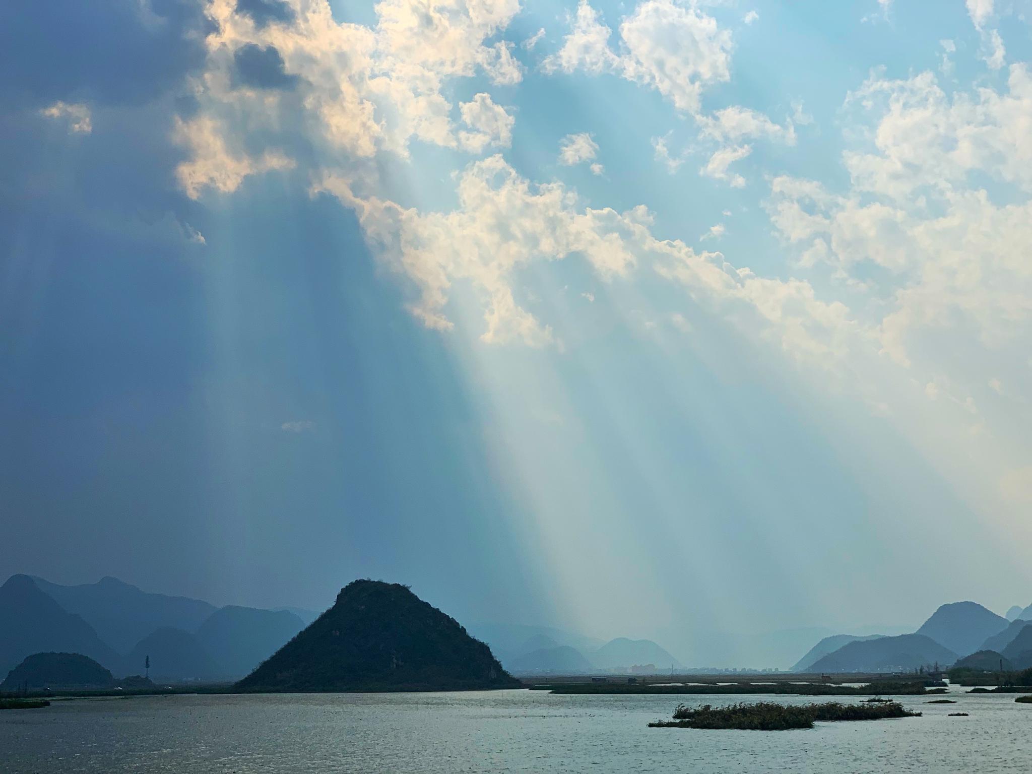 阳光穿过云层洒向湖面清水沿着山野流向远方天空接近透明的蓝