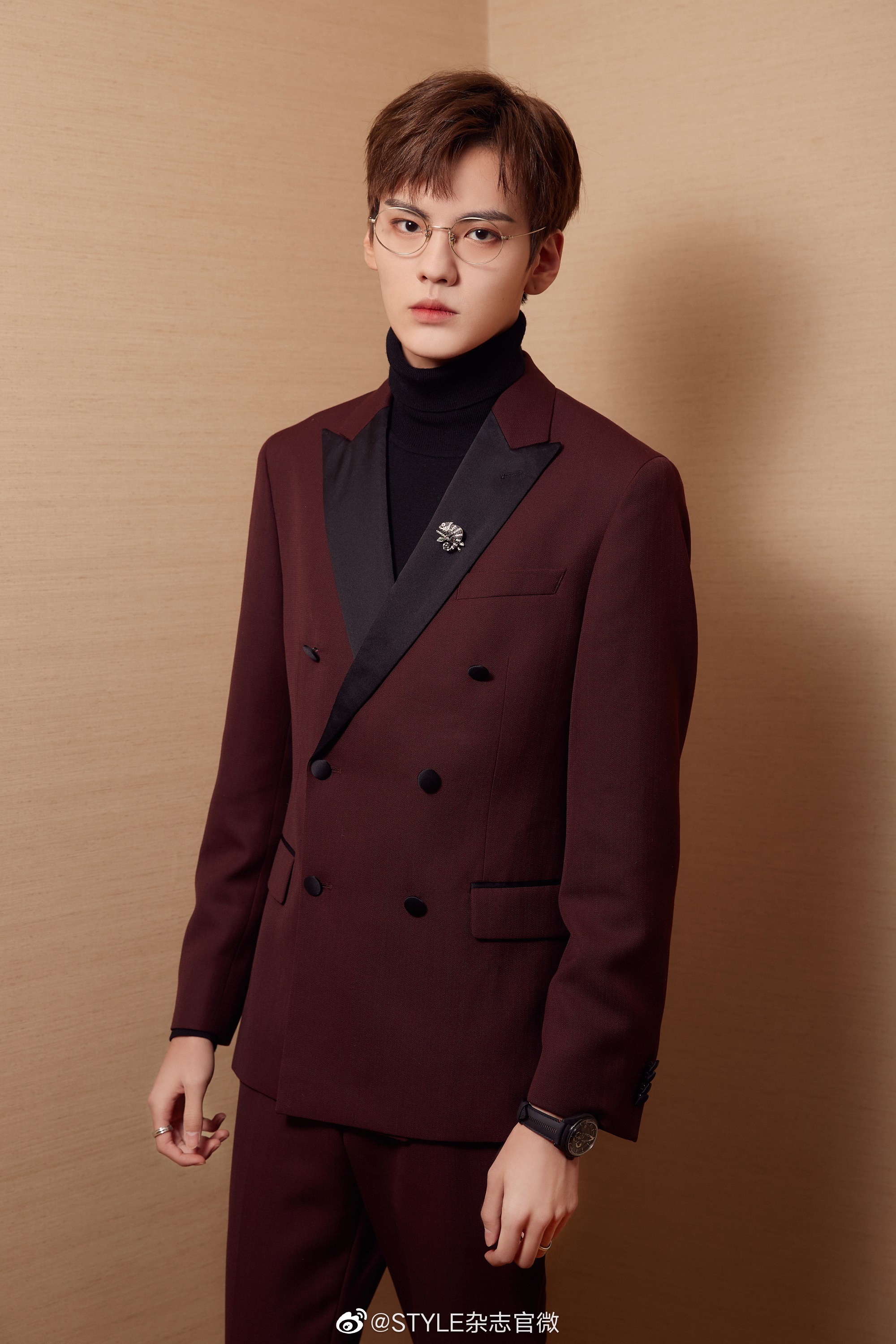 将简约的酒红色西装穿搭在身,佩戴复古框架金丝眼镜