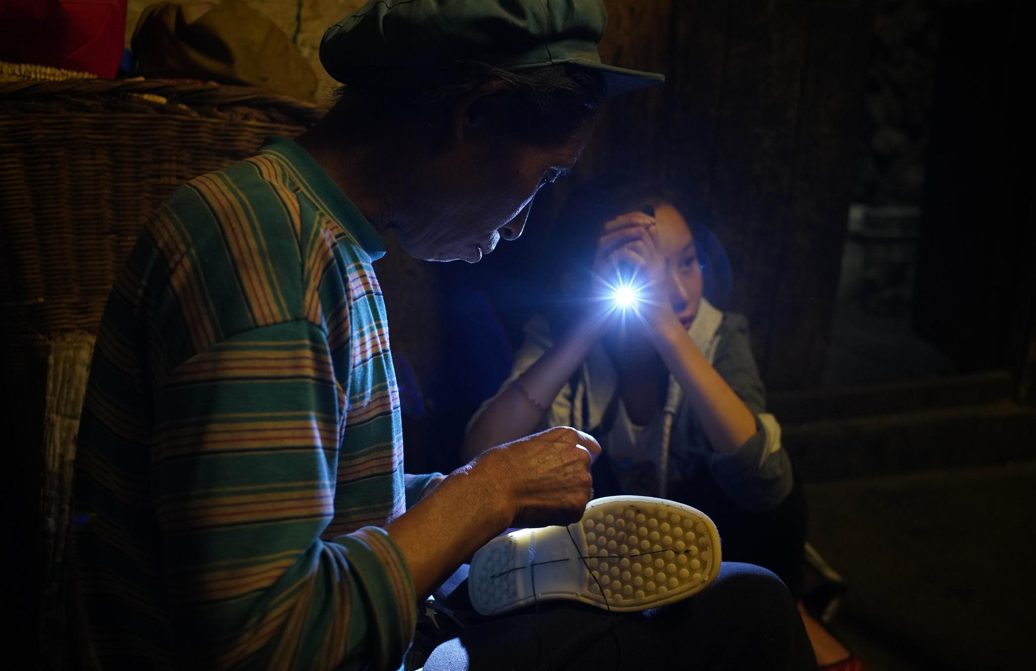 4 月27 日，陈庆花在给女儿卯会朵缝新做的布鞋，家里电灯光线不足，卯会朵在一旁给妈妈打着手电。