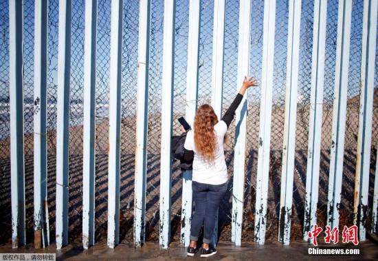 资料图：当地时间2018年12月8日，墨西哥女子Claudia Alvarez站在美墨边境墙墨西哥一侧向美国圣地亚哥一侧的老公和儿子打招呼。Alvarez说，五年来，她一直试图获得赴美签证，但她的签证申请被拒绝了。