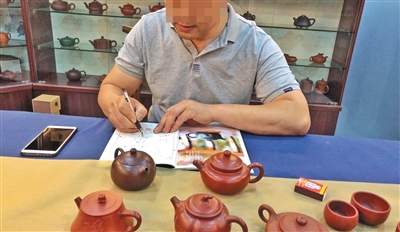 　6月20日，宜兴中国陶都陶瓷城的一家门店内，店主拿出一把“代工壶”后，又拿出一张空白的收藏证书，模仿国家工艺美术师徐某的字迹“签售”。A10-A11版摄影/新京报记者 郑新洽